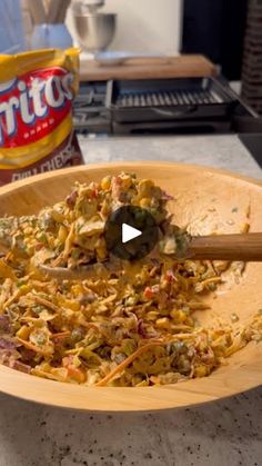 a wooden bowl filled with food on top of a counter next to a bag of chips