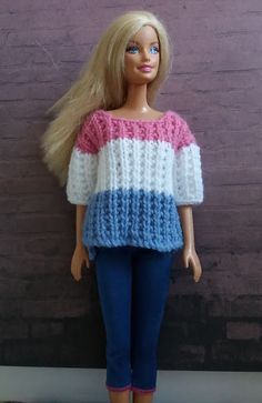 a barbie doll with blonde hair wearing a colorful sweater and jeans, standing next to a brick wall