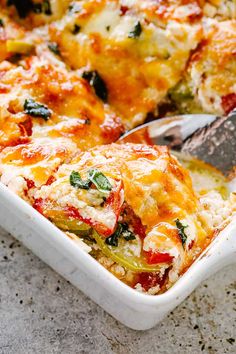 a casserole dish with cheese, vegetables and spinach being cut by a spatula