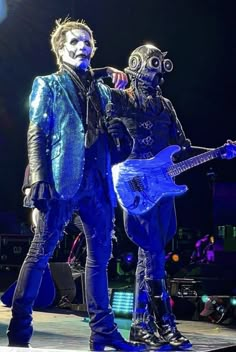 two people dressed as aliens on stage with guitars