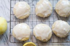 lemon cookies with icing on a cooling rack next to two lemons and an orange