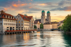 a river runs through the center of several old buildings with towers in the background at sunset