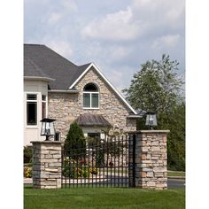 a stone house with a black iron fence and gate in front of it, surrounded by lush green grass