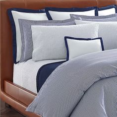 a bed with blue and white comforters on top of it in a room next to a brown leather headboard