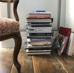 a stack of books sitting on top of a wooden floor next to a chair and window