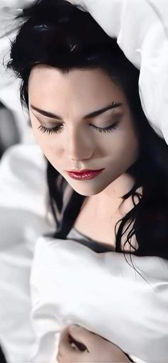 a woman with black hair and red lipstick is hiding under a white sheet in bed