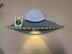 a lamp that is on the side of a wall with a green alien hat on it