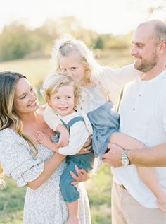 a group of people standing around each other in a field with one holding a baby