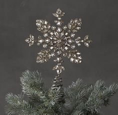 a silver snowflake decoration on top of a pine tree in front of a gray background