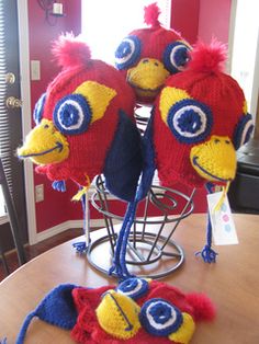 three knitted hats with blue and yellow eyes on top of a wooden table in front of a red wall