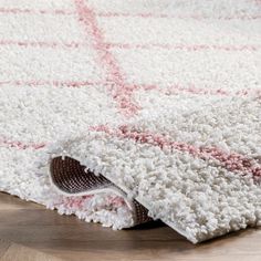 a white rug with pink and red designs on the bottom is laying on top of a wooden floor