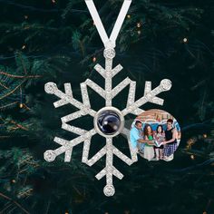 a snowflake ornament hanging from a christmas tree with two pictures on it