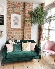 a living room filled with furniture and a brick wall behind the green couch is a potted palm tree