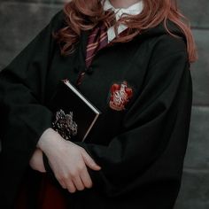 a woman with red hair wearing a harry potter robe and holding a book in her hands