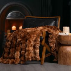 a chair with a fur blanket on it next to a wooden table and candle holders