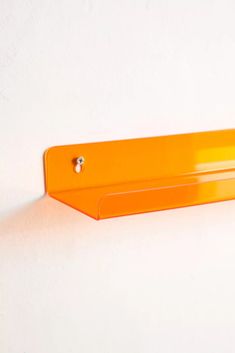 an orange plastic shelf on a white wall with a small metal object hanging from it's side