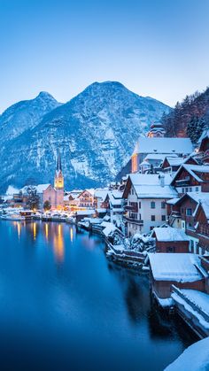 snow covered buildings line the shore of a lake with mountains in the background at dusk