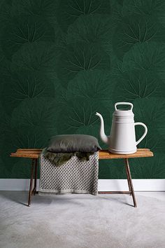 a table with a white teapot sitting on top of it next to a green wall