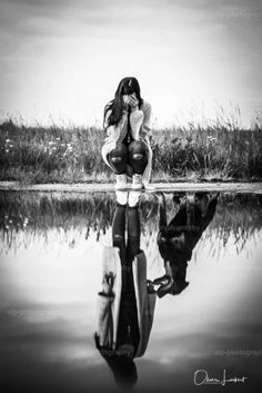 a woman sitting on the edge of a body of water with her reflection in the water