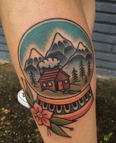 a snow globe with a house in the middle and mountains behind it on someone's leg