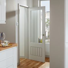 an open door leading to a kitchen with white cabinets and wood flooring on the side