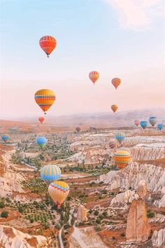 many hot air balloons are flying in the sky over some hills and valleys with trees