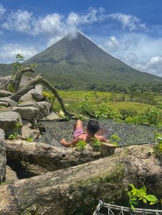 a woman laying on top of a fallen tree in front of a mountain covered in clouds