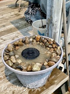 a bucket filled with rocks and water on top of a wooden table next to a potted plant