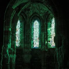 two stained glass windows in an old stone building with moss growing on the walls and floor