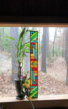 a stained glass window with plants on the windowsill and trees in the back ground