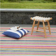 a striped rug with a wooden stool and pillow on it next to a stone wall