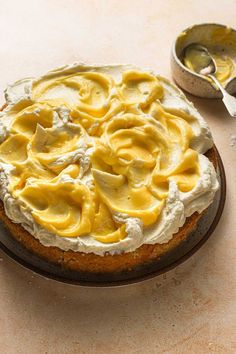 a cake with yellow icing sitting on top of a table next to a bowl