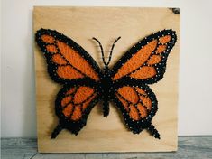 an orange and black butterfly sitting on top of a wooden plaque with beaded edges