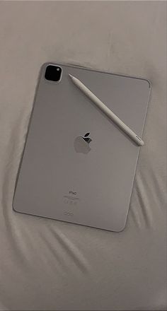 an ipad with a pen on top of it sitting on a white bed sheet next to a pillow