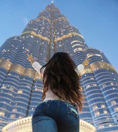 a woman standing in front of a very tall building with her arms up and legs spread out