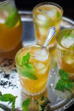 three glasses filled with different types of drinks on a tray next to another glass full of ice and mint