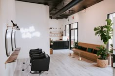 a room with white walls and wooden flooring has chairs, couches, and potted plants