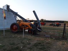 an old tractor is parked in front of a building with other vehicles behind it on the grass