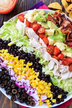 a salad with black olives, tomatoes, lettuce, corn and bacon