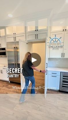 a woman is standing in the middle of a kitchen with white cabinets and wood floors