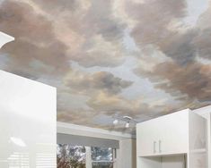 a kitchen with clouds painted on the ceiling and white cupboards in front of it