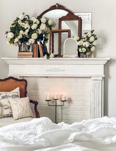 a white fireplace with flowers and candles on it in front of a mirror over a bed