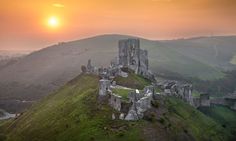 the sun is setting over an old castle on top of a hill in the countryside