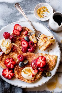 pancakes topped with fruit and butter on a white plate next to a cup of coffee