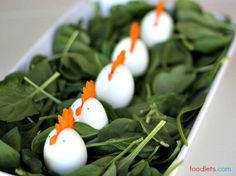 small eggs with carrot tops are arranged in a row on top of spinach leaves