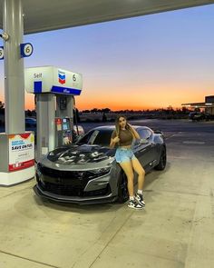 a woman standing next to a car at a gas station