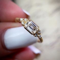 a woman's hand holding a ring with an emerald and white diamond on it