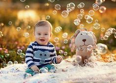 a baby sitting on the ground with bubbles in front of him and a stuffed animal