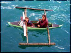 two people in a green boat on the water with sticks sticking out of it's sides