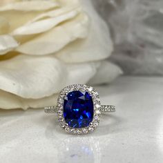 a ring with a large blue stone surrounded by white stones and diamonds on a table next to a flower